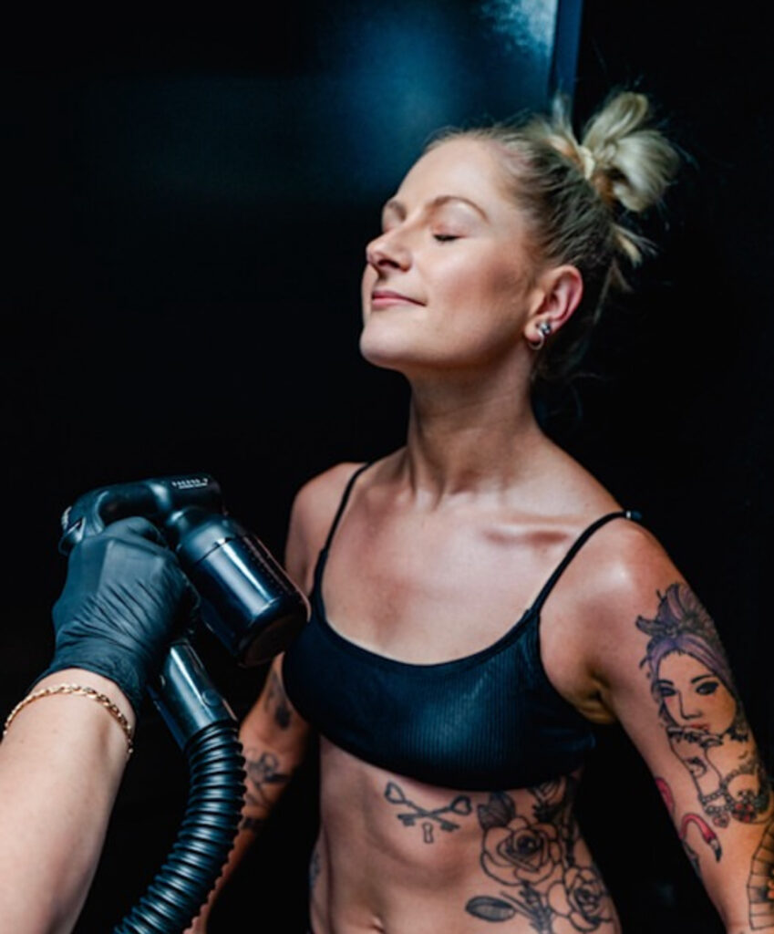woman getting professional spray tan on the front of her body at a salon